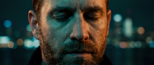 Young adult male with reddish-brown beard and fair complexion, eyes closed in contemplation against blurred city lights. Suitable for mental health, stress, depression, and wellness concepts.