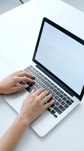 Hands typing on laptop computer keyboard at white desk workspace for remote work and digital productivity.