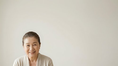 Mature woman with short gray hair and fair complexion smiling at camera against neutral background, suitable for healthcare, wellness, senior lifestyle and corporate portraits.