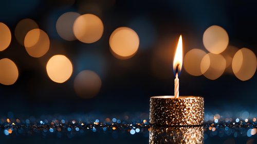 Glowing golden candle with sparkling glitter decoration against dark background with soft bokeh lights creating magical festive atmosphere.
