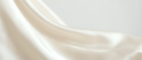 Luxurious cream silk fabric with elegant flowing folds and soft draping texture for premium fashion design and sophisticated interior decor projects.