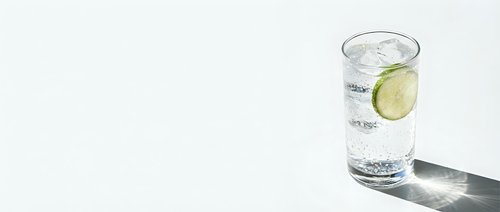 Refreshing glass of sparkling water with lime slice on white background casting shadow. Clean hydration concept for wellness and healthy lifestyle.