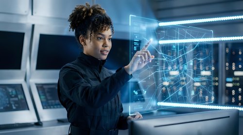 Young female engineer with curly dark hair and medium brown skin tone interacting with holographic data visualization in high-tech laboratory setting for technology and innovation concepts.