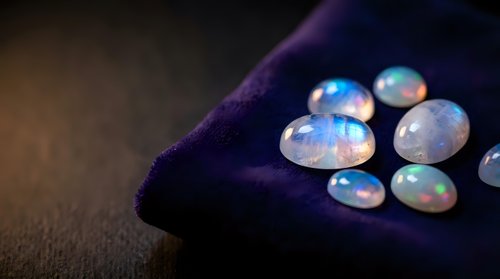 Collection of iridescent opal gemstones displaying rainbow colors on dark purple velvet fabric surface for jewelry making and luxury accessories design.