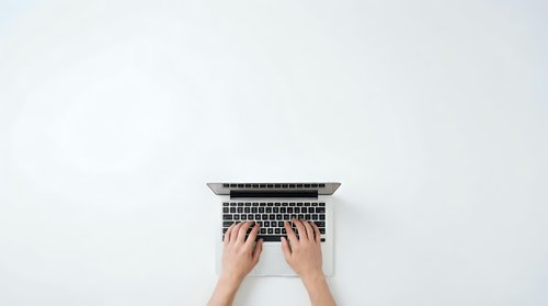 Hands typing on laptop computer from above on clean white background for business and technology concepts.