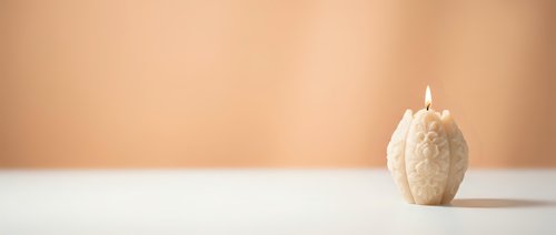 Minimalist beige textured candle burning on white surface against warm peach background for spa relaxation home decor and wellness lifestyle concepts.