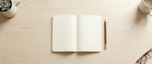 Open notebook with blank pages on wooden desk with pen, eyeglasses, coffee cup and plant for writing, planning, journaling and creative work projects.