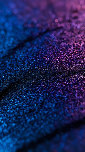 Shimmering blue and purple glitter particles create magical cosmic texture with bokeh effect, macro shot showing detailed sparkles on dark background.