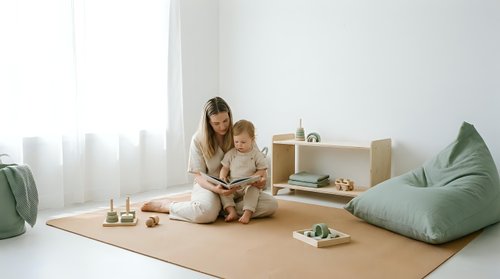 Young mother reading book with toddler in minimalist playroom with natural light and modern furniture for family bonding and early education.