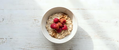 Healthy oatmeal breakfast bowl topped with fresh raspberries served in white ceramic dish on rustic wooden table background for morning meal nutrition.