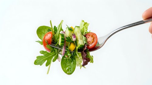 Fresh mixed greens salad with cherry tomatoes and colorful vegetables on fork against white background for healthy eating concepts.