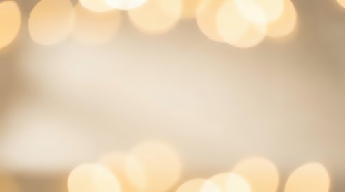 Soft golden bokeh lights creating warm ambient glow on blurred cream background for holiday celebrations, romantic events, and festive decorations.