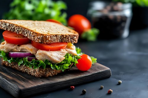 Fresh turkey sandwich with lettuce tomato and red onion on multigrain bread served on wooden cutting board for healthy lunch meal preparation.
