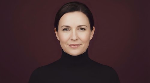 Professional middle-aged Caucasian businesswoman in black turtleneck smiling confidently against burgundy background for corporate presentations.
