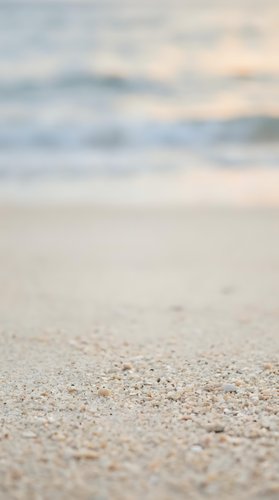 Soft sandy beach shore with gentle ocean waves and blurred seascape background, ideal for travel, vacation, and coastal lifestyle designs.