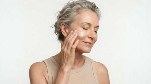 Mature Caucasian woman with gray curly hair gently touching face with closed eyes, skincare routine concept for anti-aging beauty and wellness products.