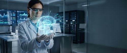 Female scientist in white lab coat examines glowing holographic brain projection in modern research laboratory, exploring neuroscience and AI technology.