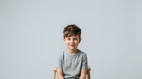 Young boy with brown hair and fair complexion wearing gray t-shirt, smiling at camera against white background. Studio portrait suitable for family, education, and lifestyle design projects.