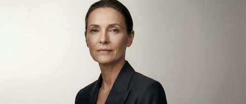 Confident mature Caucasian businesswoman in dark blazer posing against neutral background, conveying authority and professionalism.