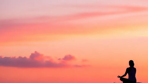 Silhouette of person meditating at sunset with pink orange sky clouds peaceful zen mindfulness relaxation spiritual wellness yoga practice serenity.