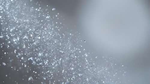 Sparkling silver glitter particles scattered on soft gray gradient background with bokeh light effects and copy space for text or design elements.
