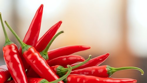 Fresh red hot chili peppers with green stems arranged on wooden surface for cooking and spicy food preparation in kitchen setting.