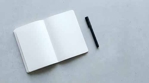 Open blank notebook with black pen on gray concrete surface, ready for writing, planning, or design mockups.