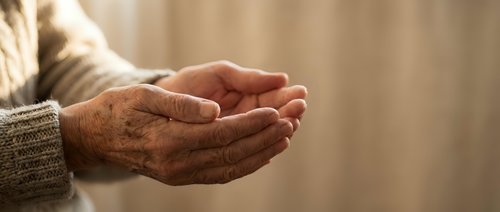 Elderly hands cupped together in prayer or meditation gesture, showing wrinkled skin and age spots. Concept of spirituality, hope, faith, and senior wellness.
