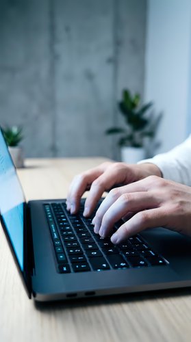 Professional hands typing on laptop keyboard in modern office workspace with plants and marble wall background for business productivity.