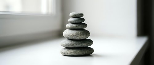 Balanced stack of smooth river stones creating zen meditation tower on white surface near window with natural light for mindfulness and wellness concepts.