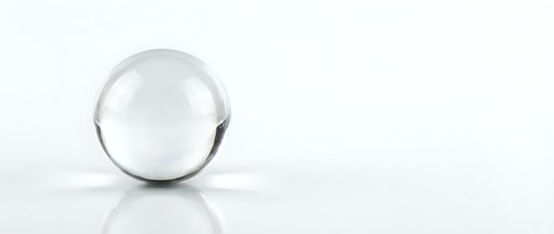 Clear glass sphere on white reflective surface with soft lighting and minimalist composition for modern design projects.