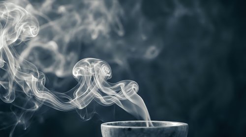 White smoke swirls rising from cup creating elegant flowing patterns against dark background for aromatherapy and relaxation concepts.