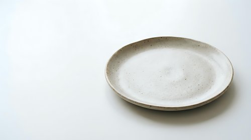 Empty ceramic plate with speckled glaze on white background, minimalist tableware for food presentation and kitchen styling projects.