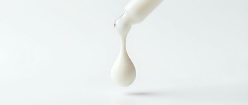 Milk pouring from bottle creating droplet against white background, suitable for dairy product packaging and advertising designs.