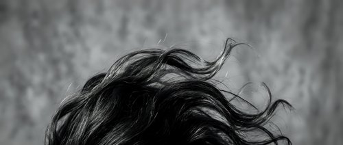 Dramatic black and white portrait of flowing hair in motion against textured background. Hair movement and dynamic styling concept for beauty campaigns.