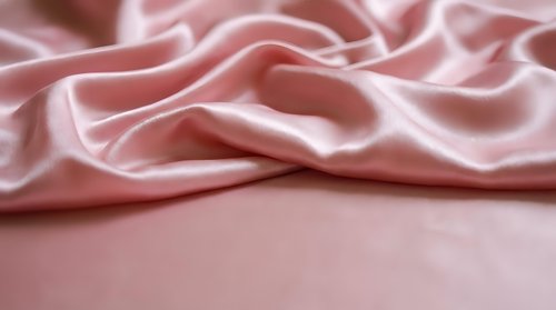 Soft pink silk fabric with elegant flowing folds and luxurious texture for fashion design, textile backgrounds, and romantic decor projects.
