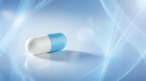 Blue and white medical capsule pill on reflective surface with soft blue light rays background for healthcare and pharmaceutical concepts.