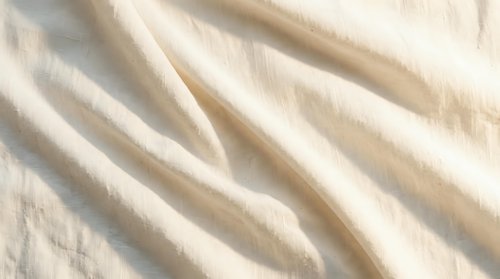 Soft cream colored fabric with elegant flowing folds and gentle waves creating luxurious textile background for fashion and interior design projects.
