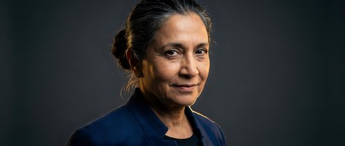 Professional mature Hispanic businesswoman in navy blazer with confident expression against dark background for corporate presentations.