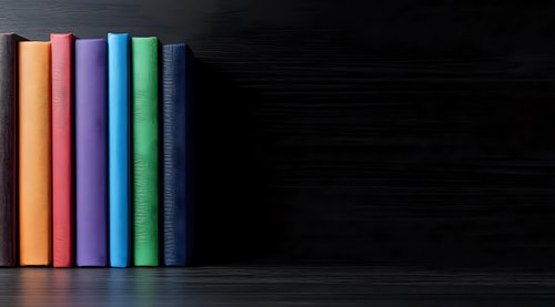Colorful hardcover books standing in row against dark background, creating minimalist composition with vibrant spines in orange, purple, green and blue tones.