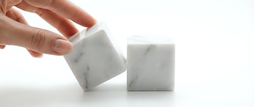 Hand reaching for white marble cube blocks on clean surface for modern minimalist design and architectural concept projects.