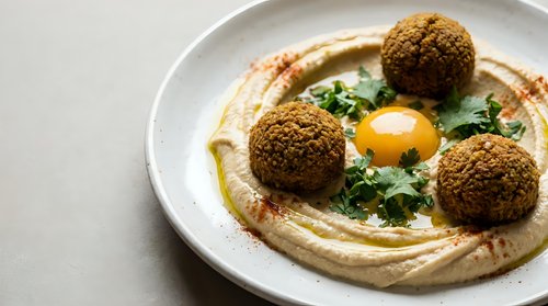 Creamy hummus topped with crispy falafel balls, fresh herbs and olive oil drizzle served on white plate for Mediterranean cuisine and healthy eating.