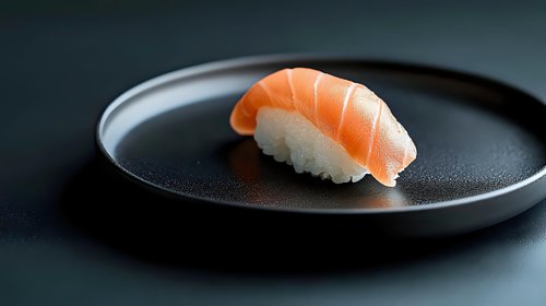Fresh salmon nigiri sushi piece on black ceramic plate against dark background, minimalist Japanese cuisine presentation with soft natural lighting.