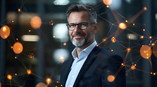 Confident mature businessman with gray beard and glasses smiling against digital network visualization with glowing orange bokeh lights in corporate office.