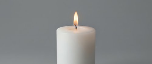 White pillar candle burning with bright flame on neutral gray background for relaxation, meditation, spa treatments, aromatherapy and home decor concepts.