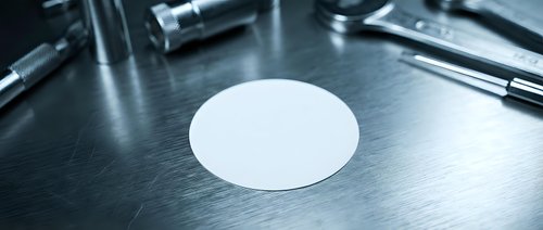 White round blank label sticker on metallic surface with medical instruments in background for product branding and identification purposes.