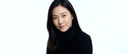 Young Asian woman in black turtleneck sweater smiling warmly at camera against white background. Professional headshot for business and lifestyle content.
