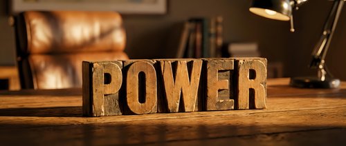 Wooden block letters spelling POWER on a rustic desk with warm bokeh background, evoking strength, leadership, and motivation in a cozy office setting.