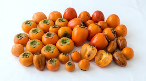 Fresh orange persimmons arranged on white background, whole and sliced fruits showing vibrant color and texture, suitable for food photography, culinary design, and healthy eating content.