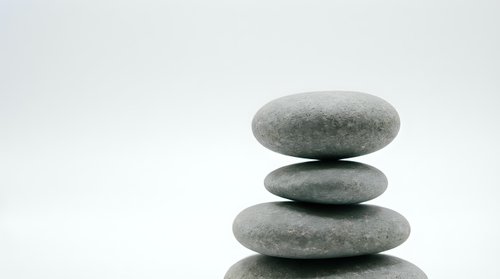 Stacked smooth gray stones balanced in zen tower formation on white background, isolated for wellness and meditation design projects.